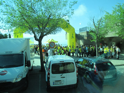 Photo was taken from a parking lot, looking at a yellow inflated arch about 40 feet high with black sillouettes of a person with a cane. standing in a line going under the arch are dozens of people, about half of them are wearing bright yellow shirts.